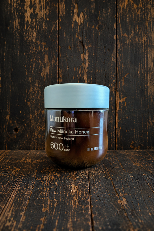 Manukora Raw Manuka Honey MGO 600+ on dark wood background